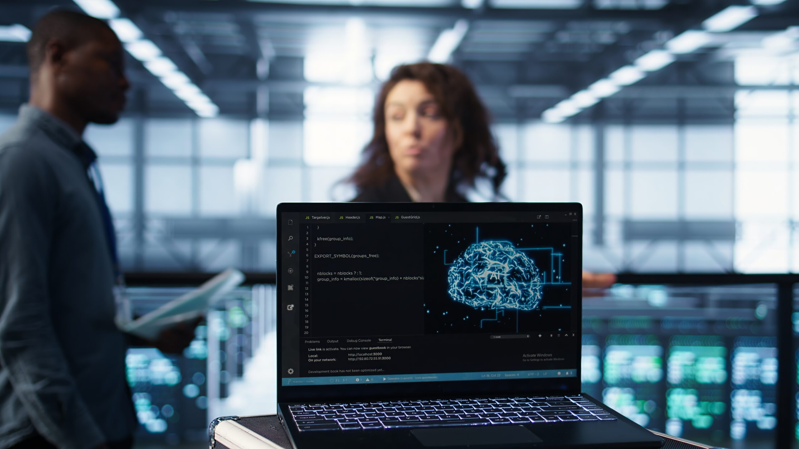 Laptop in front of data center engineers in blurry background deploying artificial intelligence driven management tools. AI driven notebook used for overseeing server clusters, camera B close up